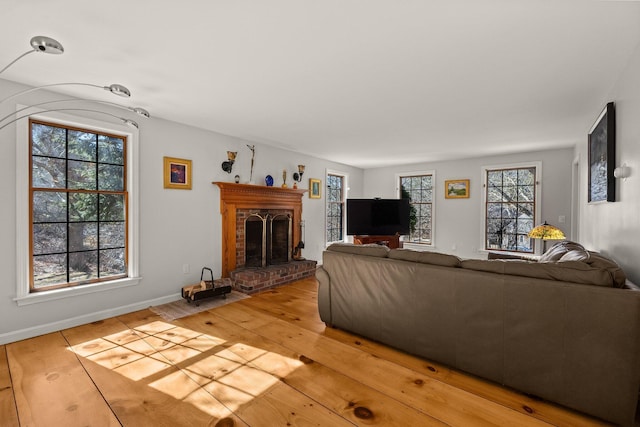 living area with light wood finished floors, a brick fireplace, and baseboards