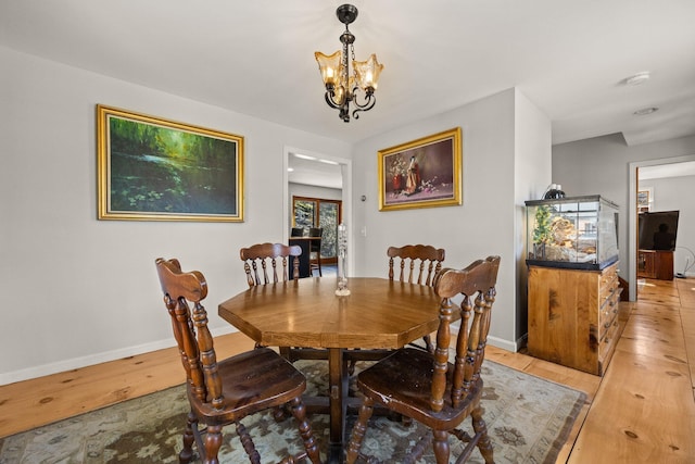 dining area with light wood finished floors, baseboards, and a notable chandelier