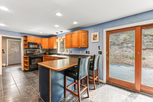 kitchen with kitchen peninsula, pendant lighting, backsplash, a breakfast bar, and black appliances