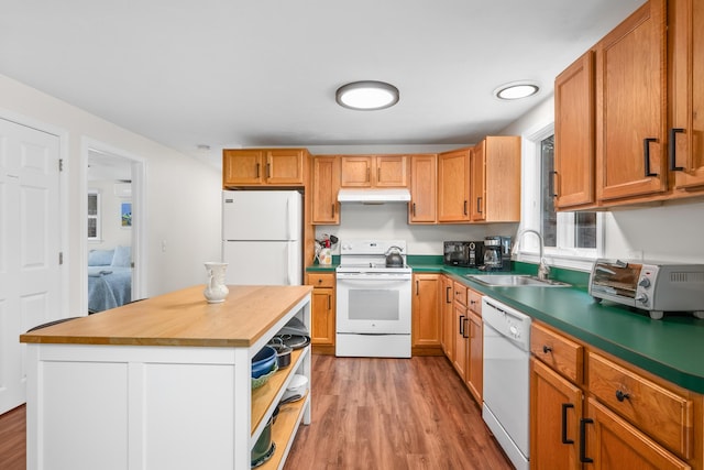 kitchen featuring under cabinet range hood, white appliances, a sink, and wood finished floors