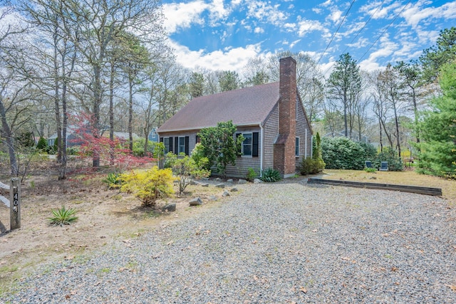 view of front facade featuring a chimney, gravel driveway, and roof with shingles