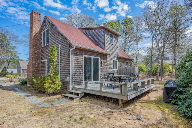 back of property featuring a deck, a shingled roof, outdoor dining space, and a chimney