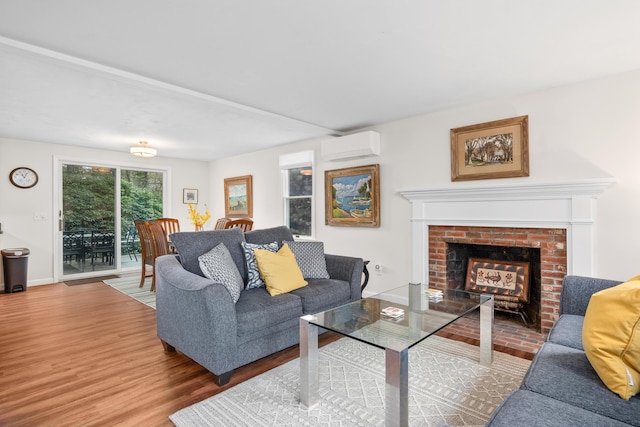 living room featuring a brick fireplace, a wall mounted AC, baseboards, and wood finished floors