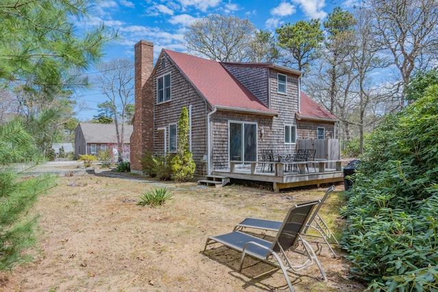 back of house with a chimney, a deck, and a shingled roof