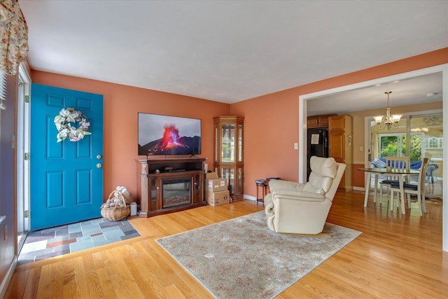 living area with a chandelier, light wood-style floors, a glass covered fireplace, and baseboards