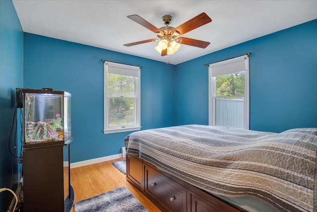 bedroom with multiple windows, baseboards, light wood-style flooring, and a ceiling fan