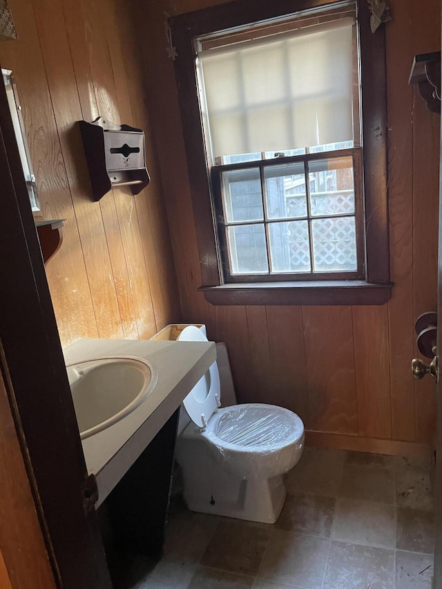 bathroom with toilet, vanity, and wooden walls