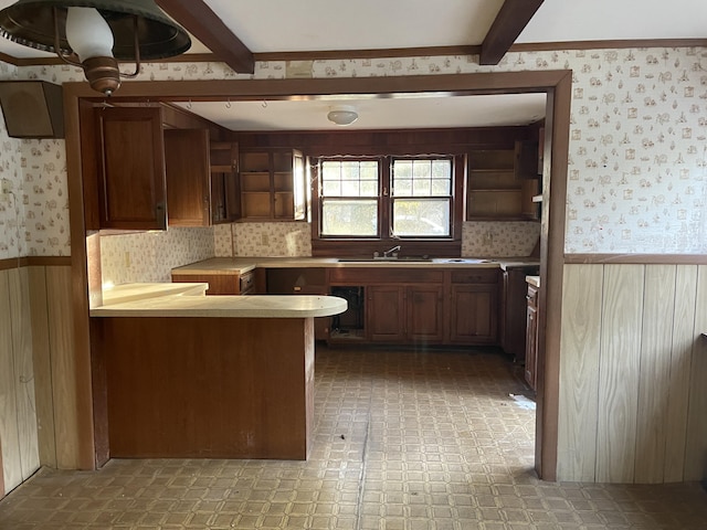 kitchen featuring kitchen peninsula, sink, wooden walls, and beamed ceiling