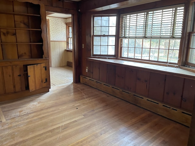 unfurnished dining area featuring light wood-type flooring, wooden walls, and a baseboard heating unit