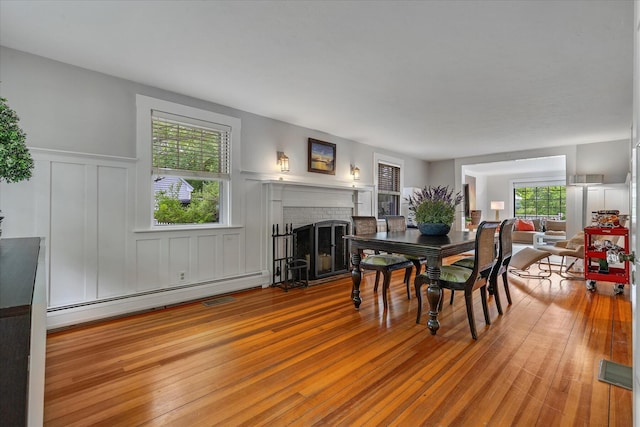 117 Parker Rd, Osterville, MA 02655 - dining room featuring a baseboard heating unit, a brick fireplace, a wainscoted wall, a decorative wall, and wood finished floors