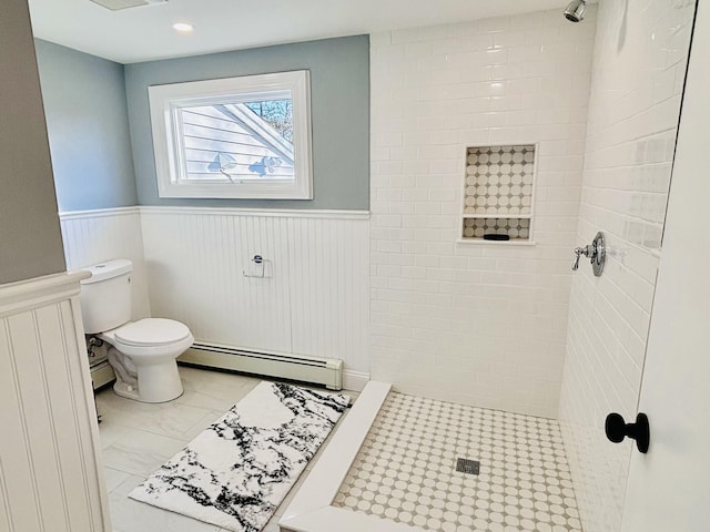 full bathroom featuring a tile shower, toilet, wainscoting, and baseboard heating