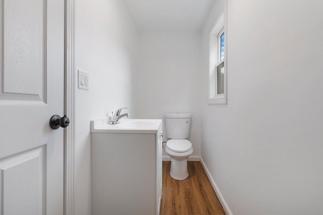 half bath featuring toilet, wood finished floors, vanity, and baseboards