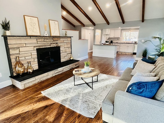 living area featuring a stone fireplace, baseboards, lofted ceiling with beams, and dark wood finished floors