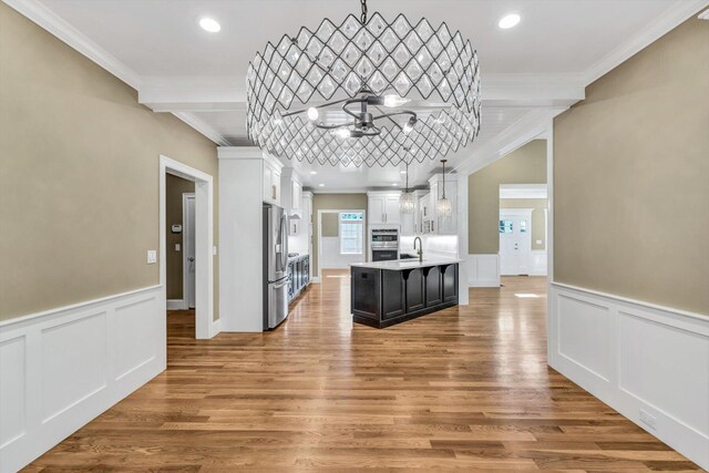 kitchen with crown molding, hardwood / wood-style floors, white cabinets, decorative light fixtures, and stainless steel appliances