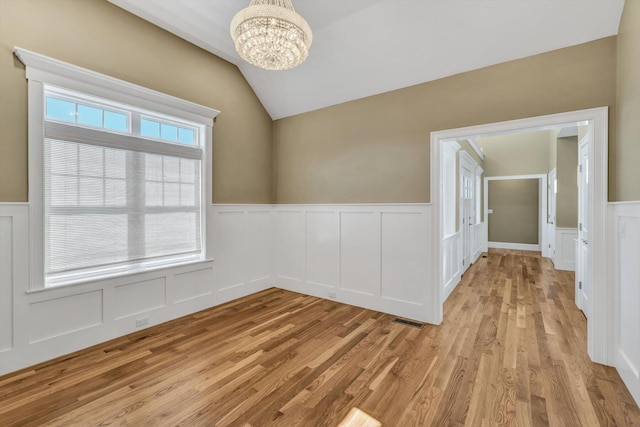 spare room featuring light wood-type flooring, vaulted ceiling, a wealth of natural light, and an inviting chandelier