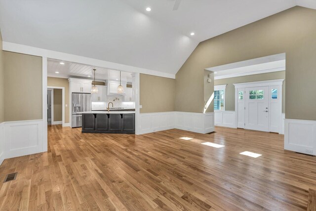 unfurnished living room featuring sink, vaulted ceiling, and light hardwood / wood-style flooring