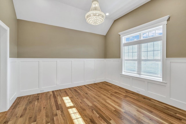 spare room with light hardwood / wood-style floors, an inviting chandelier, and vaulted ceiling