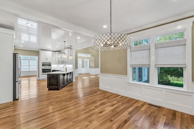 kitchen featuring crown molding, pendant lighting, white cabinets, an island with sink, and stainless steel appliances