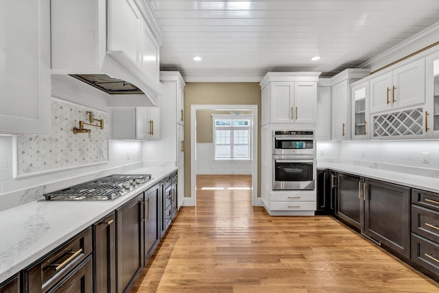 kitchen with appliances with stainless steel finishes, custom range hood, white cabinets, light hardwood / wood-style floors, and decorative backsplash