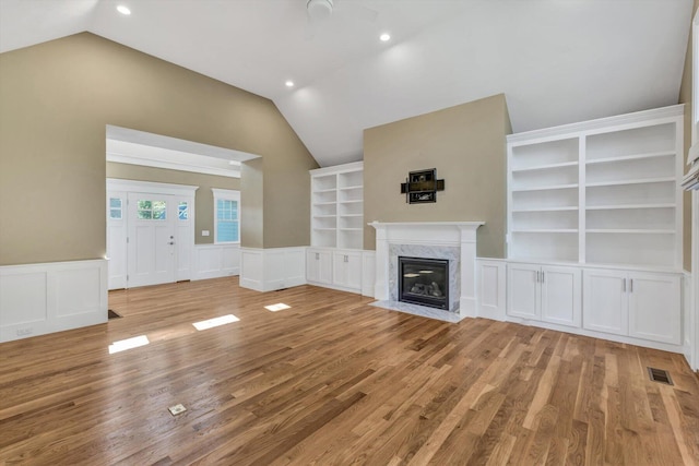 unfurnished living room featuring a fireplace, built in features, light hardwood / wood-style flooring, and lofted ceiling