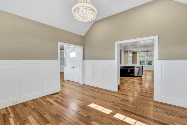 spare room featuring a notable chandelier, light wood-type flooring, and lofted ceiling