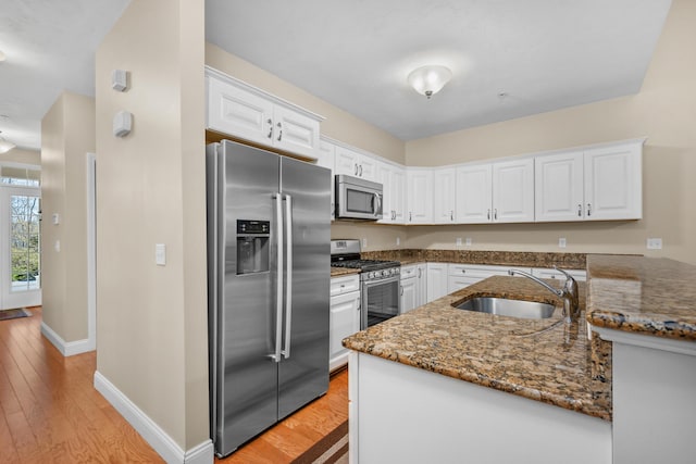 kitchen featuring white cabinets, appliances with stainless steel finishes, a sink, dark stone countertops, and baseboards