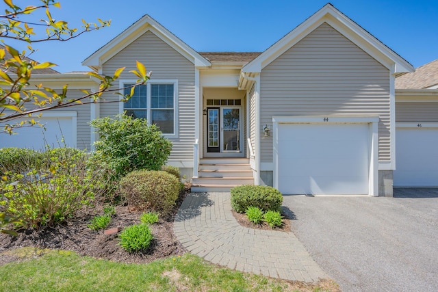 ranch-style home featuring an attached garage, roof with shingles, and aphalt driveway