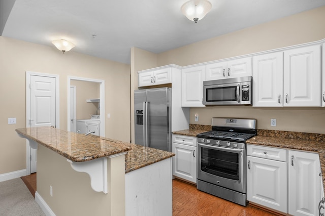 kitchen with white cabinets, a center island, dark stone counters, stainless steel appliances, and washer and clothes dryer