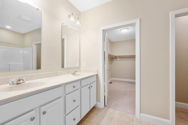 bathroom featuring double vanity, baseboards, tile patterned floors, a spacious closet, and a sink