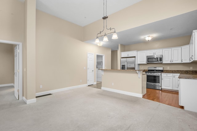 kitchen featuring a kitchen island, appliances with stainless steel finishes, baseboards, white cabinets, and light carpet