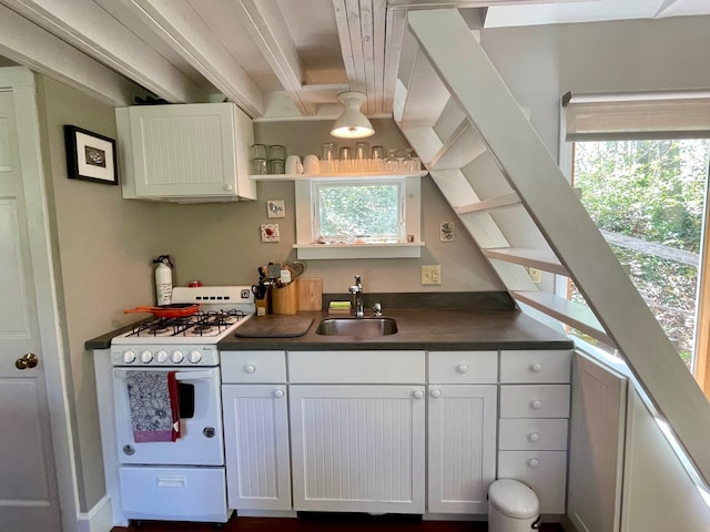 kitchen with white range with gas stovetop, a sink, dark countertops, and white cabinets