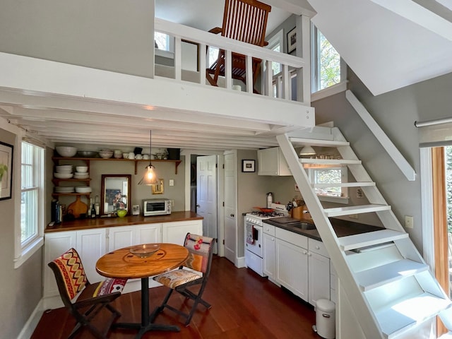 kitchen featuring white gas range, dark wood finished floors, white cabinetry, wood counters, and a high ceiling