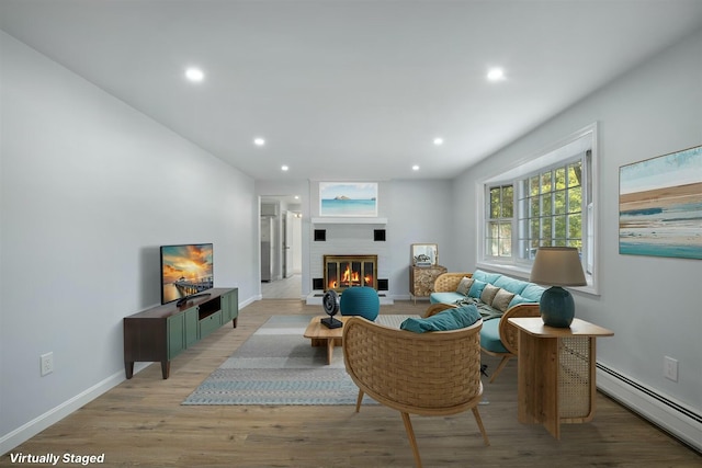 living area featuring a glass covered fireplace, baseboards, light wood-style flooring, recessed lighting, and a baseboard heating unit