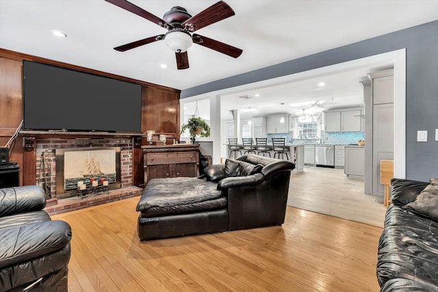 living room featuring ceiling fan, a healthy amount of sunlight, light hardwood / wood-style flooring, and a fireplace