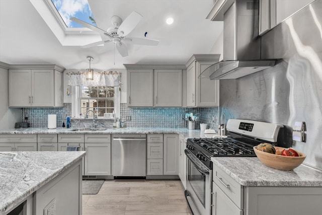 kitchen with gray cabinetry, sink, stainless steel appliances, light stone counters, and wall chimney exhaust hood