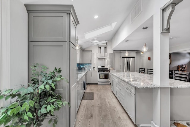 kitchen with wall chimney range hood, stainless steel appliances, gray cabinetry, and tasteful backsplash