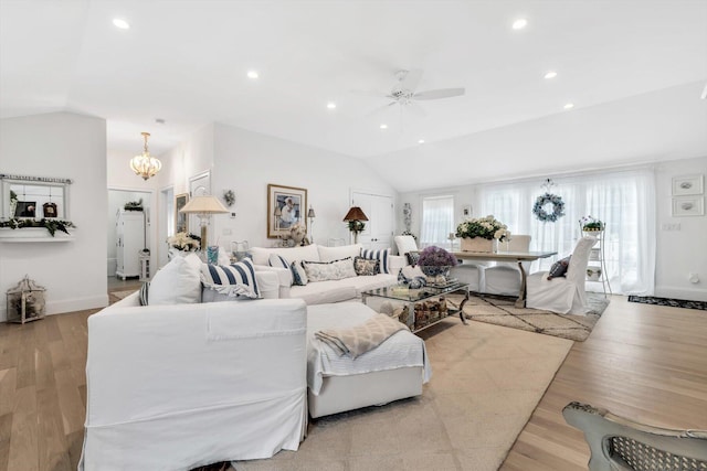 living room with light wood-type flooring, ceiling fan with notable chandelier, and vaulted ceiling