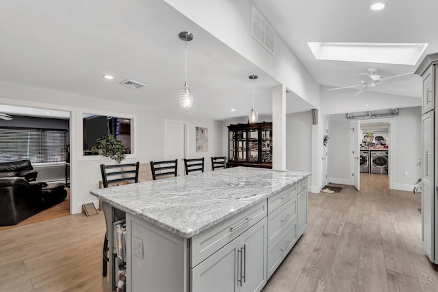 kitchen featuring a center island, a kitchen breakfast bar, pendant lighting, washing machine and dryer, and light stone counters