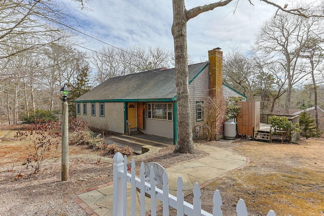 view of front facade with entry steps, a fenced front yard, roof with shingles, a wooden deck, and a chimney