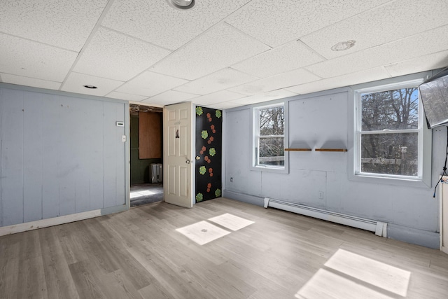 spare room with a paneled ceiling, baseboard heating, and wood finished floors