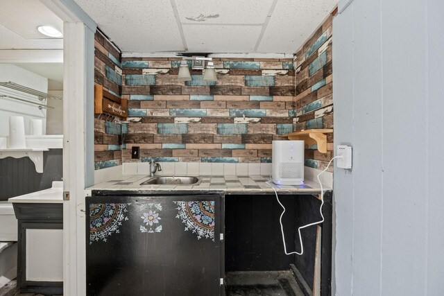 kitchen with wood walls, a paneled ceiling, and a sink