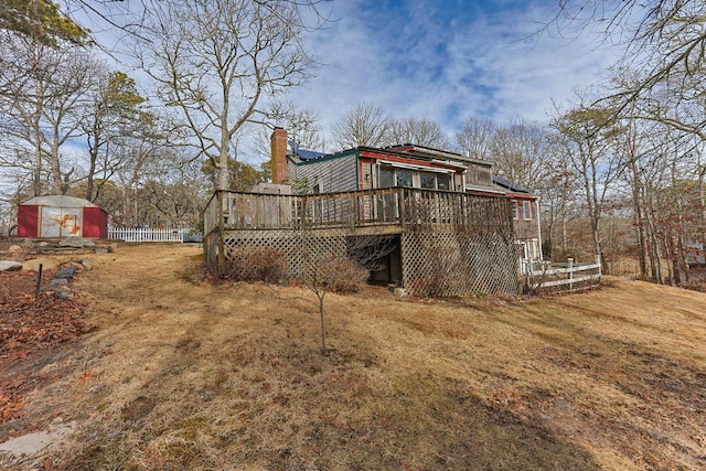 back of house with fence, a chimney, an outdoor structure, a storage unit, and a deck