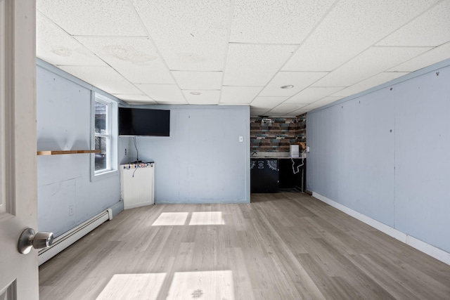 unfurnished living room featuring a drop ceiling, a baseboard heating unit, baseboards, and wood finished floors