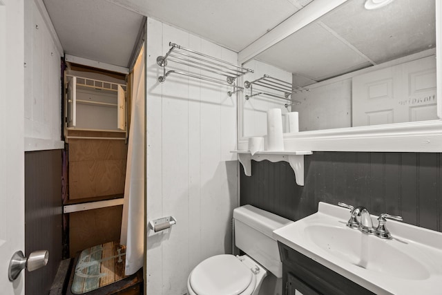 bathroom featuring wood walls, toilet, and vanity