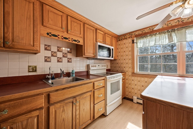 kitchen with white appliances, wallpapered walls, a sink, a baseboard heating unit, and brown cabinets