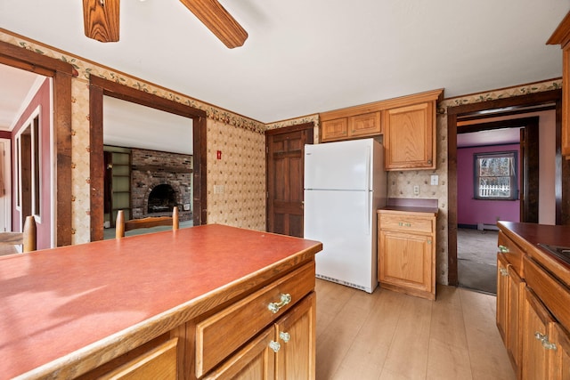 kitchen with wallpapered walls, freestanding refrigerator, light wood-style floors, dark countertops, and a brick fireplace