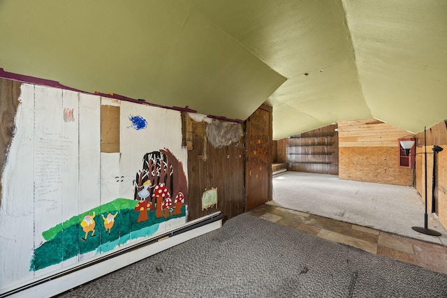 interior space featuring vaulted ceiling, stone finish flooring, wood walls, and a baseboard radiator