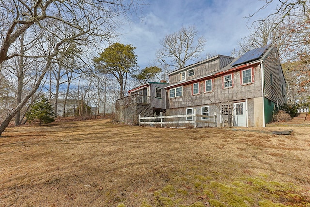 back of house with roof mounted solar panels and a lawn