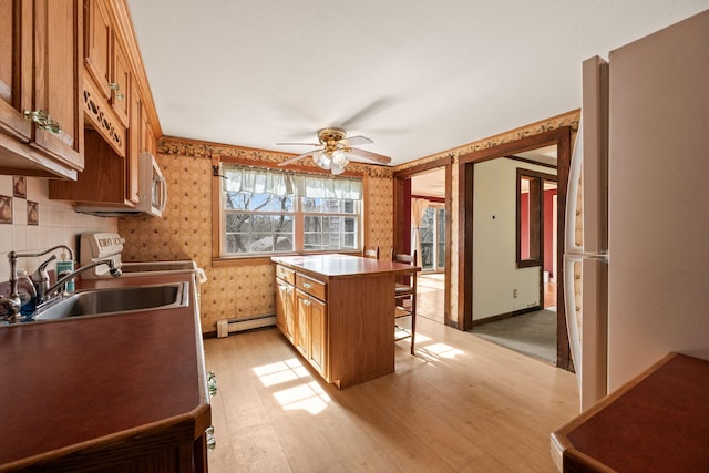 kitchen with light wood-style flooring, a sink, stainless steel microwave, a baseboard heating unit, and wallpapered walls