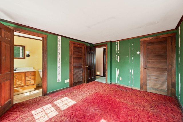 unfurnished bedroom with ornamental molding, ensuite bathroom, a sink, a closet, and carpet floors